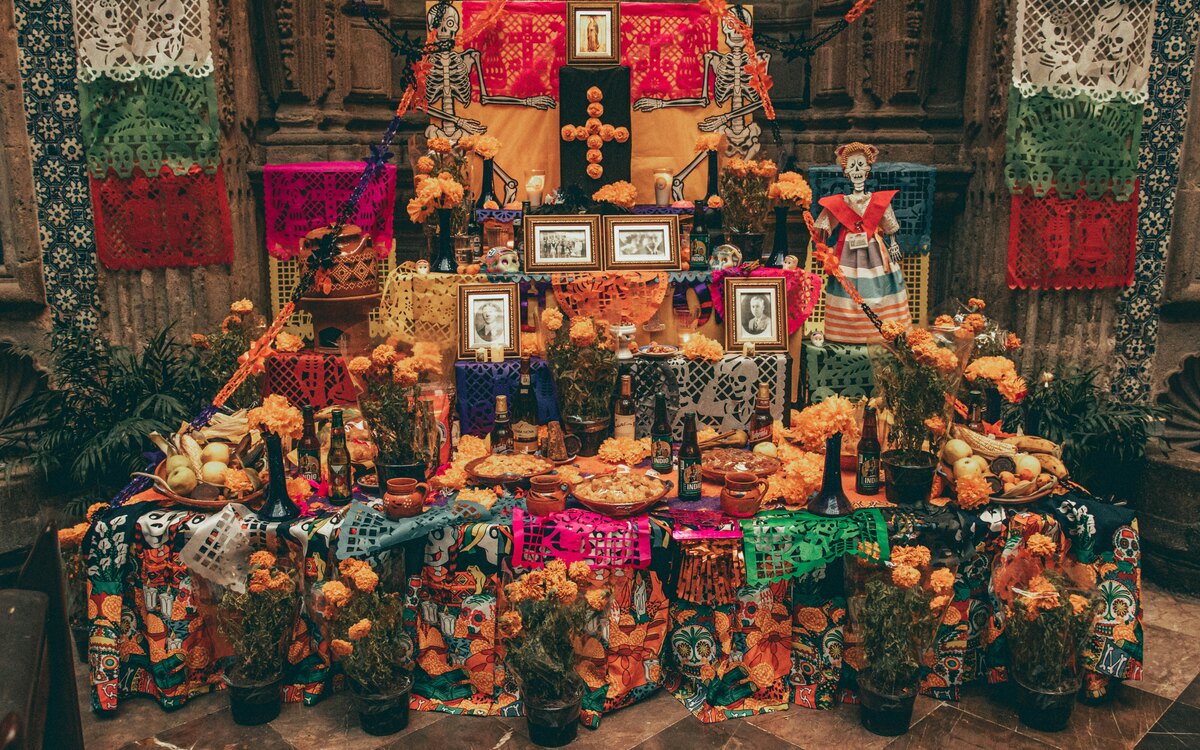 A richly decorated Day of the Dead ofrenda with marigolds, papel picado, candles, photographs, food and drink